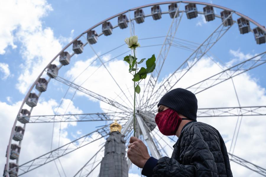 Man with face mask and flower in front of Brussels ferris wheel.